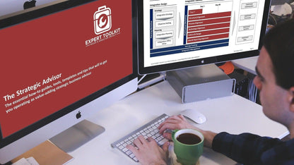 A business consultant types at a desk equipped with two monitors and a keyboard. The left screen displays a red background featuring information on "The Strategic Advisor" along with its logo, suggesting a strategic advantage. The right screen presents a table titled "Integration Design, Integration Plan." A green mug is placed on the desk.