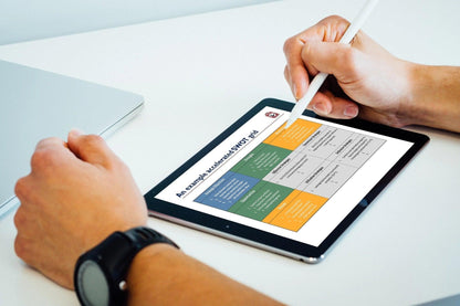 A business consultant uses a stylus to tap on The Strategic Advisor, a tablet showcasing a SWOT analysis chart with quadrants for Strengths, Weaknesses, Opportunities, and Threats. Sporting an elegant wristwatch and accompanied by a silver laptop on the white table, they delve into strategic advantages.